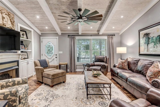 living area featuring beam ceiling, a fireplace, ceiling fan, wood finished floors, and wooden ceiling