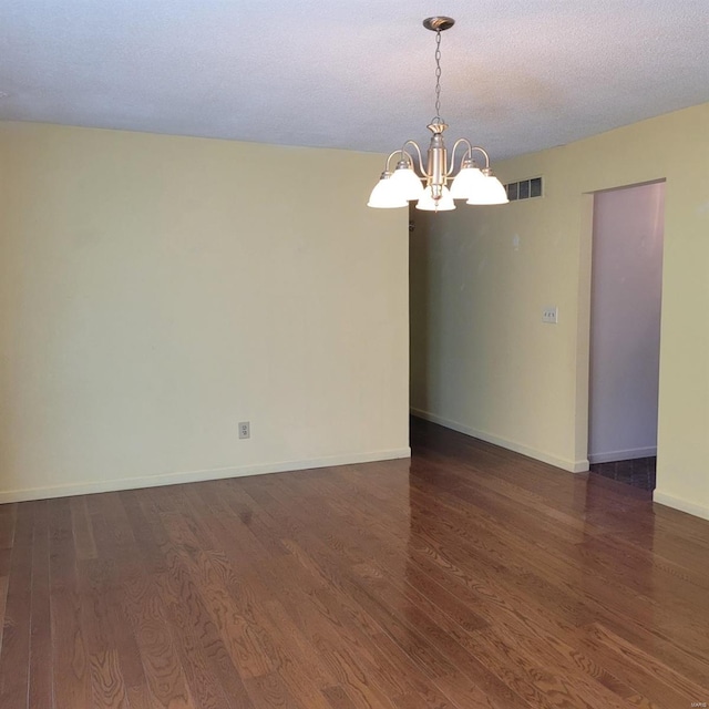 empty room with dark hardwood / wood-style flooring, a textured ceiling, and a notable chandelier