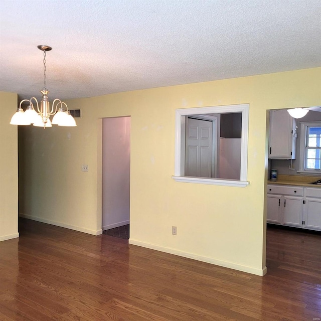 spare room with a textured ceiling, a notable chandelier, and dark wood-type flooring