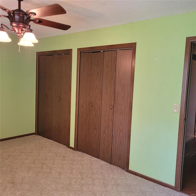 unfurnished bedroom featuring ceiling fan, light colored carpet, a textured ceiling, and two closets