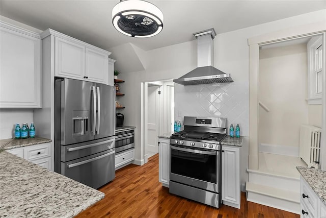 kitchen with radiator, wall chimney range hood, dark hardwood / wood-style floors, white cabinets, and appliances with stainless steel finishes