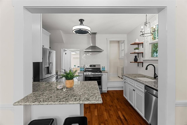 kitchen with a kitchen bar, stainless steel appliances, sink, wall chimney range hood, and white cabinetry