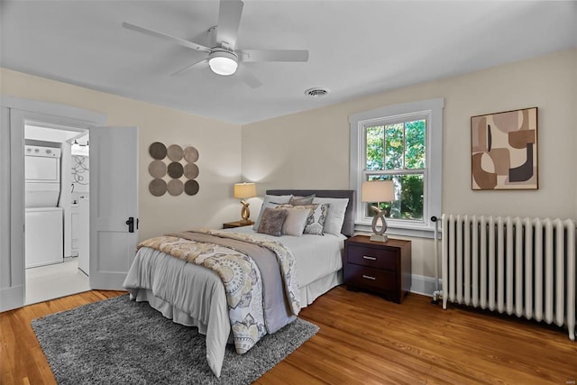 bedroom with connected bathroom, radiator, ceiling fan, stacked washer / drying machine, and light wood-type flooring