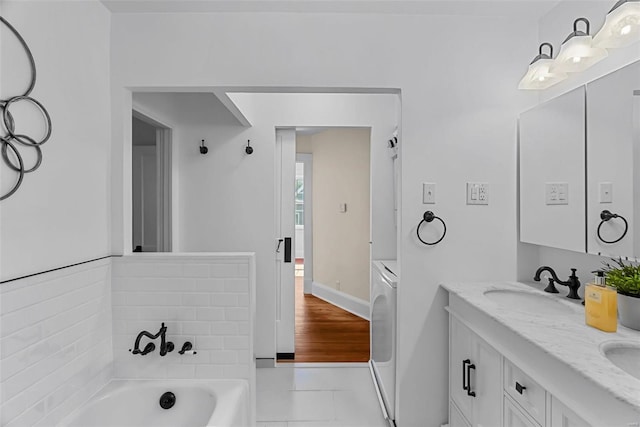 bathroom with tile patterned floors, a bathtub, washer / clothes dryer, and vanity