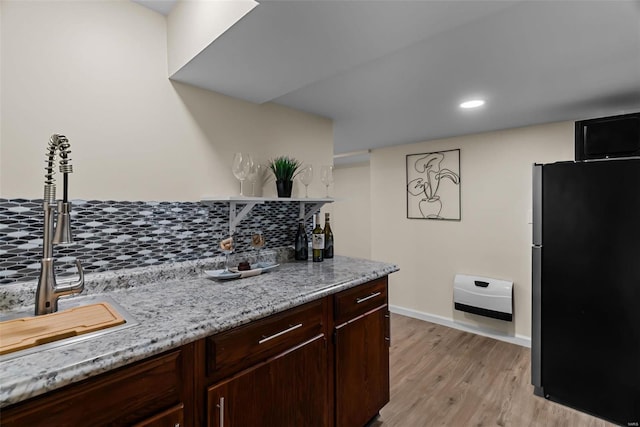 kitchen with dark brown cabinetry, light stone countertops, sink, refrigerator, and light wood-type flooring