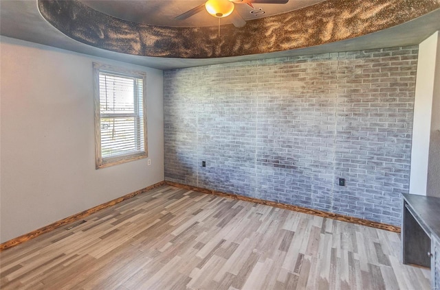 unfurnished room with light hardwood / wood-style floors, brick wall, and ceiling fan