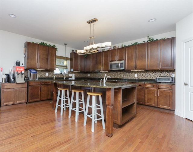 kitchen featuring a breakfast bar, decorative light fixtures, a center island with sink, light hardwood / wood-style floors, and backsplash