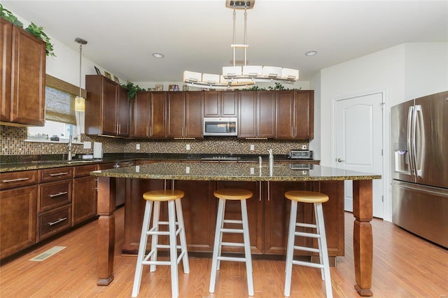 kitchen featuring stainless steel appliances, dark stone countertops, a center island with sink, and decorative light fixtures