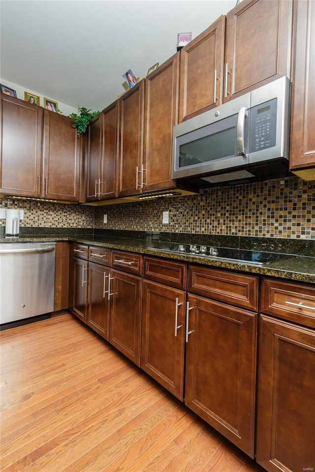 kitchen with backsplash, light hardwood / wood-style flooring, dark stone counters, and appliances with stainless steel finishes