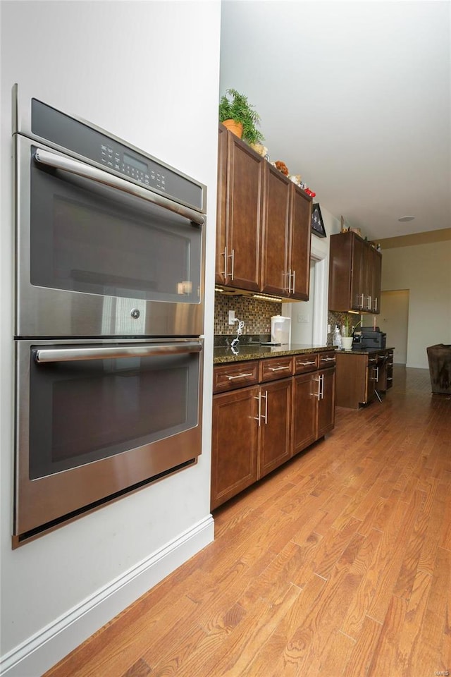 kitchen featuring backsplash, light hardwood / wood-style flooring, dark stone counters, and stainless steel double oven