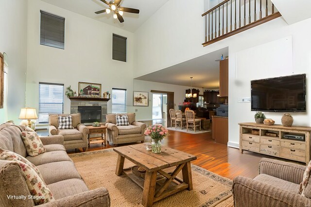 living room featuring wood-type flooring, a towering ceiling, and ceiling fan with notable chandelier