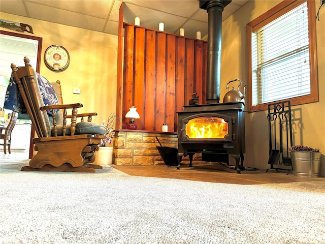 living area featuring carpet flooring, a drop ceiling, and a wood stove