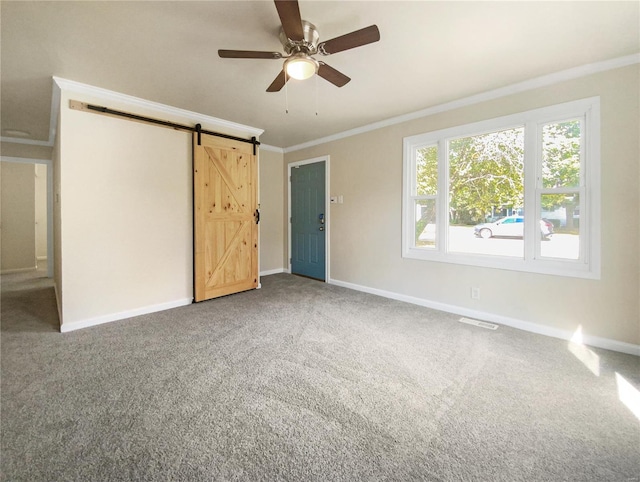 unfurnished bedroom with ceiling fan, carpet floors, crown molding, and a barn door