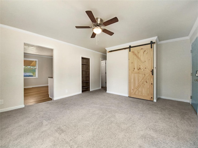 unfurnished bedroom featuring a barn door, crown molding, ceiling fan, and light colored carpet