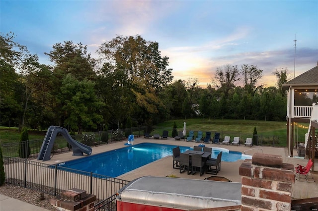 pool at dusk with a patio, a water slide, and a lawn