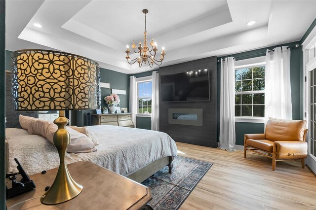 bedroom featuring light wood-type flooring, a tray ceiling, a large fireplace, and an inviting chandelier