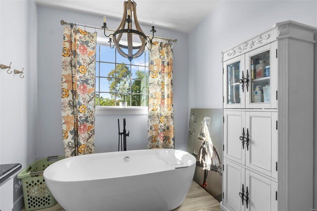 bathroom with an inviting chandelier, a washtub, and wood-type flooring