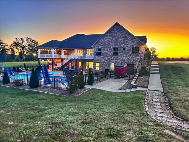 back house at dusk featuring a patio and a lawn