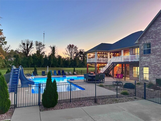 pool at dusk featuring a water slide and a patio area