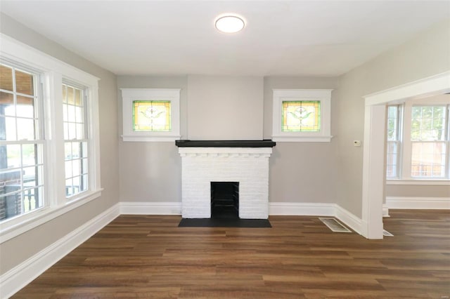 unfurnished living room featuring a fireplace, plenty of natural light, and dark wood-type flooring