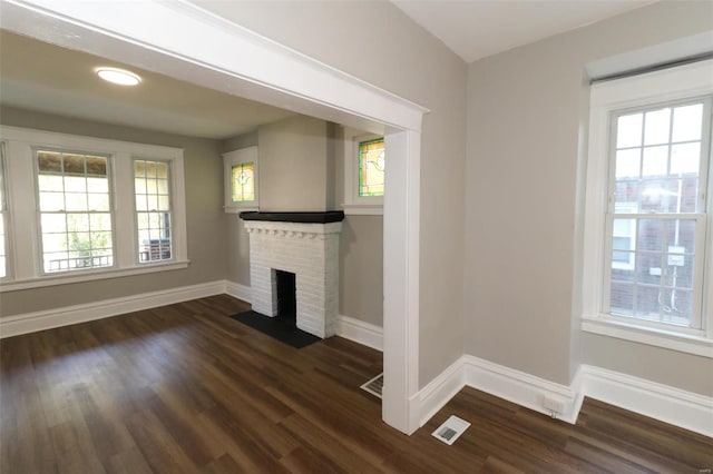 unfurnished living room featuring a fireplace, plenty of natural light, and dark wood-type flooring