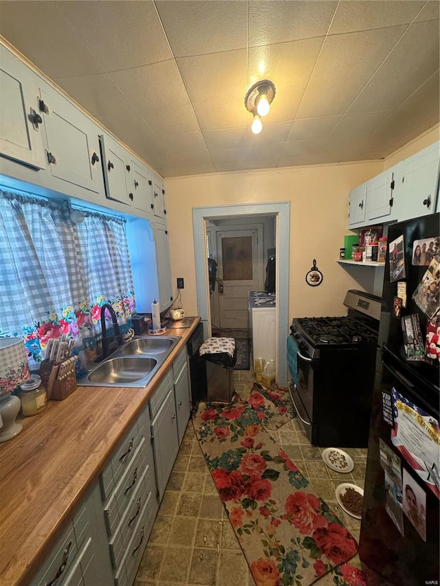 kitchen featuring independent washer and dryer, white cabinets, butcher block countertops, black appliances, and sink