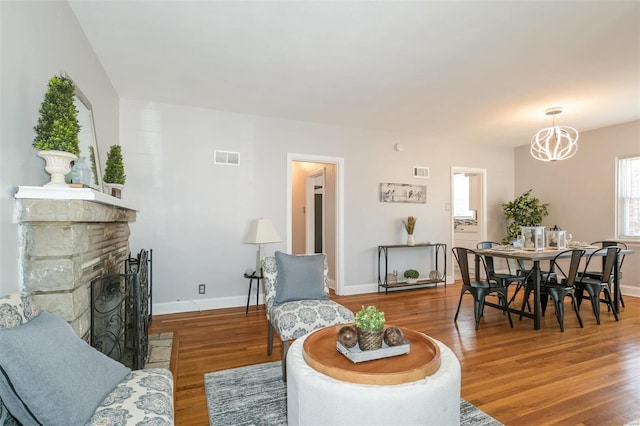 living room with wood-type flooring, a chandelier, and a stone fireplace