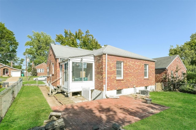 rear view of property featuring central air condition unit, a patio, a sunroom, and a lawn