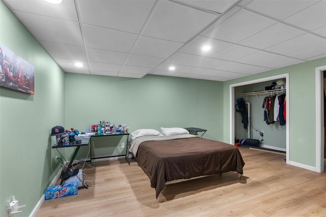 bedroom with a closet, a paneled ceiling, and light wood-type flooring