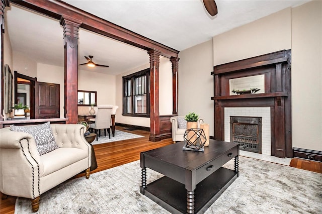 living room featuring ornate columns, wood-type flooring, a fireplace, and ceiling fan