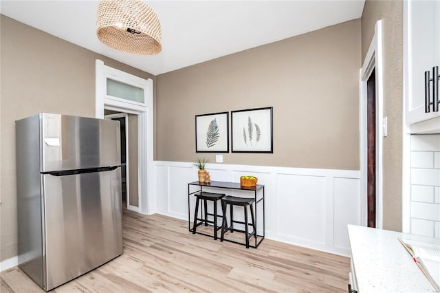 kitchen with white cabinetry, a kitchen breakfast bar, light hardwood / wood-style floors, and stainless steel refrigerator