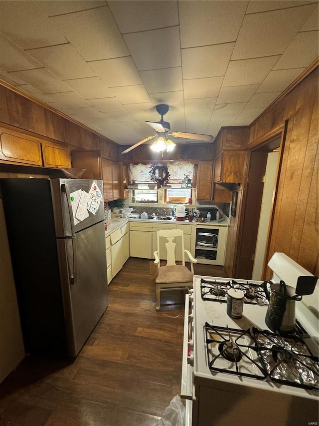 kitchen featuring ceiling fan, wood walls, stainless steel fridge, dark wood-type flooring, and white range with gas stovetop