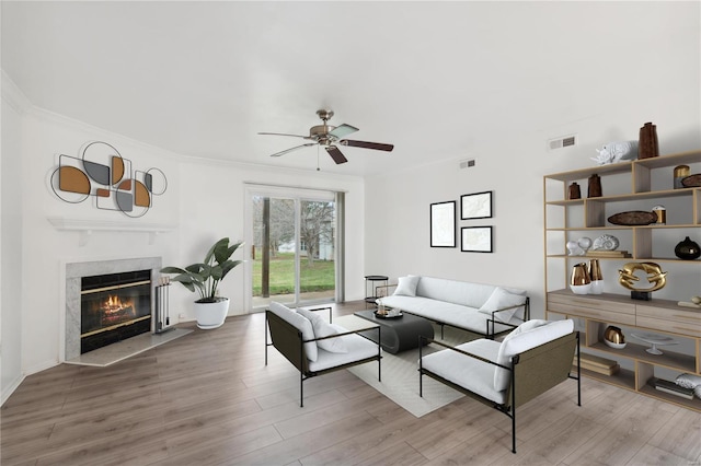 living room with a premium fireplace, hardwood / wood-style floors, ceiling fan, and crown molding