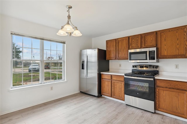 kitchen with pendant lighting, a notable chandelier, light wood-type flooring, and appliances with stainless steel finishes