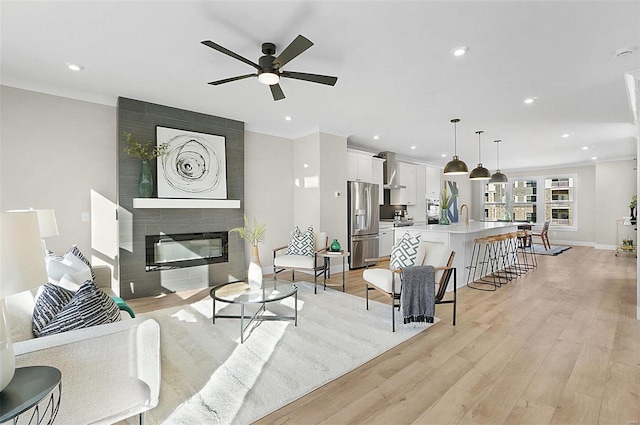 living room with ceiling fan, a fireplace, sink, and light hardwood / wood-style flooring