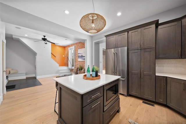 kitchen featuring dark brown cabinetry, light hardwood / wood-style flooring, hanging light fixtures, appliances with stainless steel finishes, and a kitchen bar