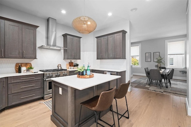 kitchen featuring high end stainless steel range, wall chimney exhaust hood, hanging light fixtures, and light hardwood / wood-style flooring