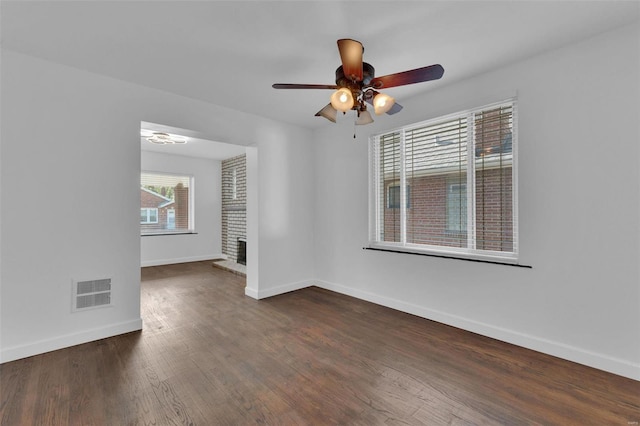 spare room featuring ceiling fan, dark hardwood / wood-style floors, and a brick fireplace