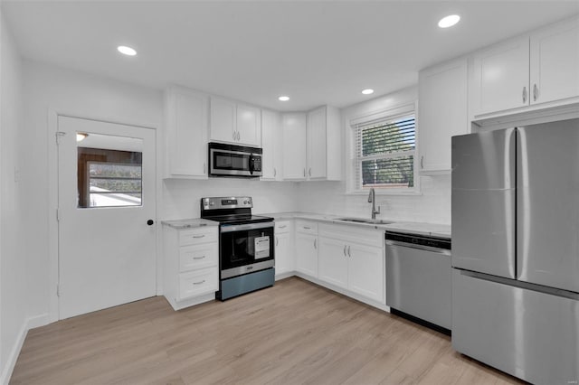 kitchen with backsplash, sink, light hardwood / wood-style flooring, white cabinetry, and stainless steel appliances