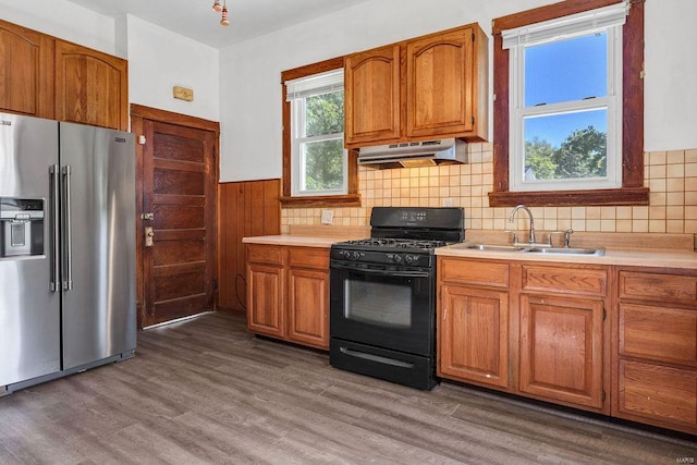 kitchen with black gas stove, hardwood / wood-style flooring, stainless steel fridge with ice dispenser, sink, and range hood