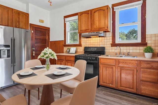 kitchen featuring black gas stove, sink, exhaust hood, stainless steel refrigerator with ice dispenser, and dark hardwood / wood-style flooring