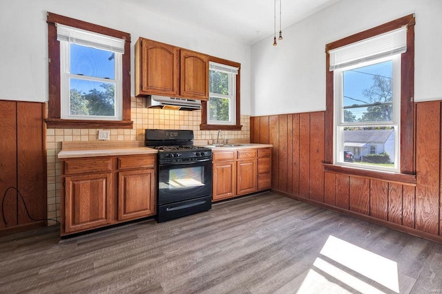 kitchen with wood walls, black gas range oven, sink, and dark hardwood / wood-style flooring