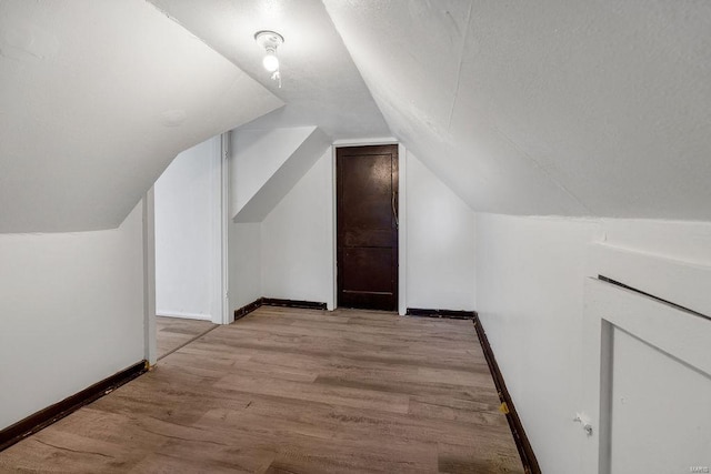 bonus room with light wood-type flooring and vaulted ceiling