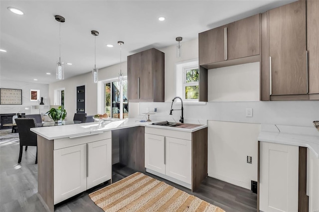 kitchen with sink, dark hardwood / wood-style floors, kitchen peninsula, decorative light fixtures, and white cabinets