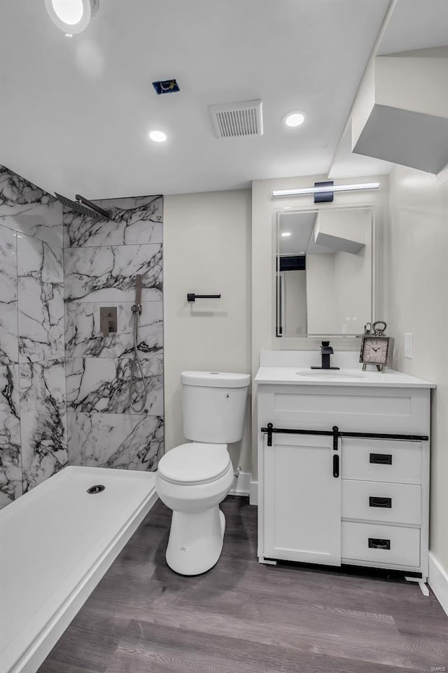 bathroom with a tile shower, hardwood / wood-style floors, toilet, vanity, and tile walls