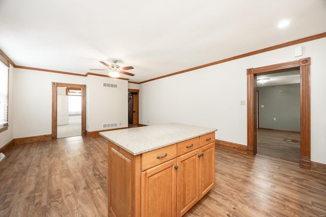 kitchen with ceiling fan, light wood-type flooring, crown molding, and a center island