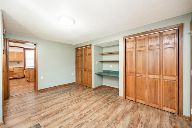 unfurnished bedroom with two closets, light hardwood / wood-style flooring, and built in desk