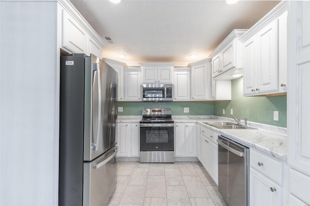 kitchen with appliances with stainless steel finishes, light stone counters, sink, and white cabinets