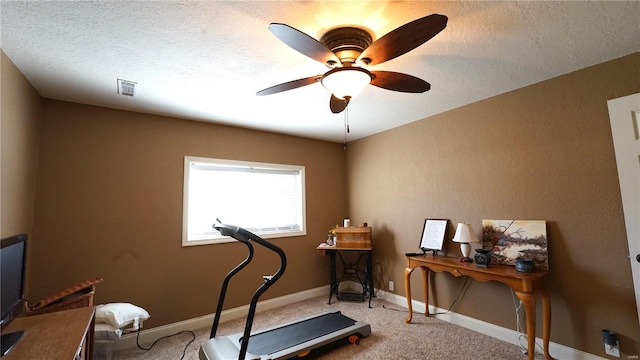 exercise room featuring ceiling fan, carpet floors, and a textured ceiling