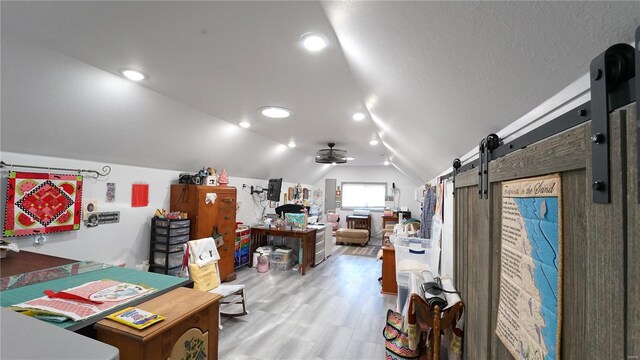 office area with ceiling fan, a barn door, light wood-type flooring, and lofted ceiling